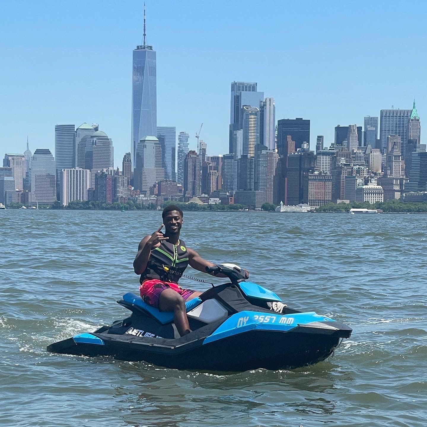 Jet ski rental near NYC — rider on a WaveRunner with Manhattan skyline and One World Trade Center in background, perfect birthday or Father's Day experience near New York City